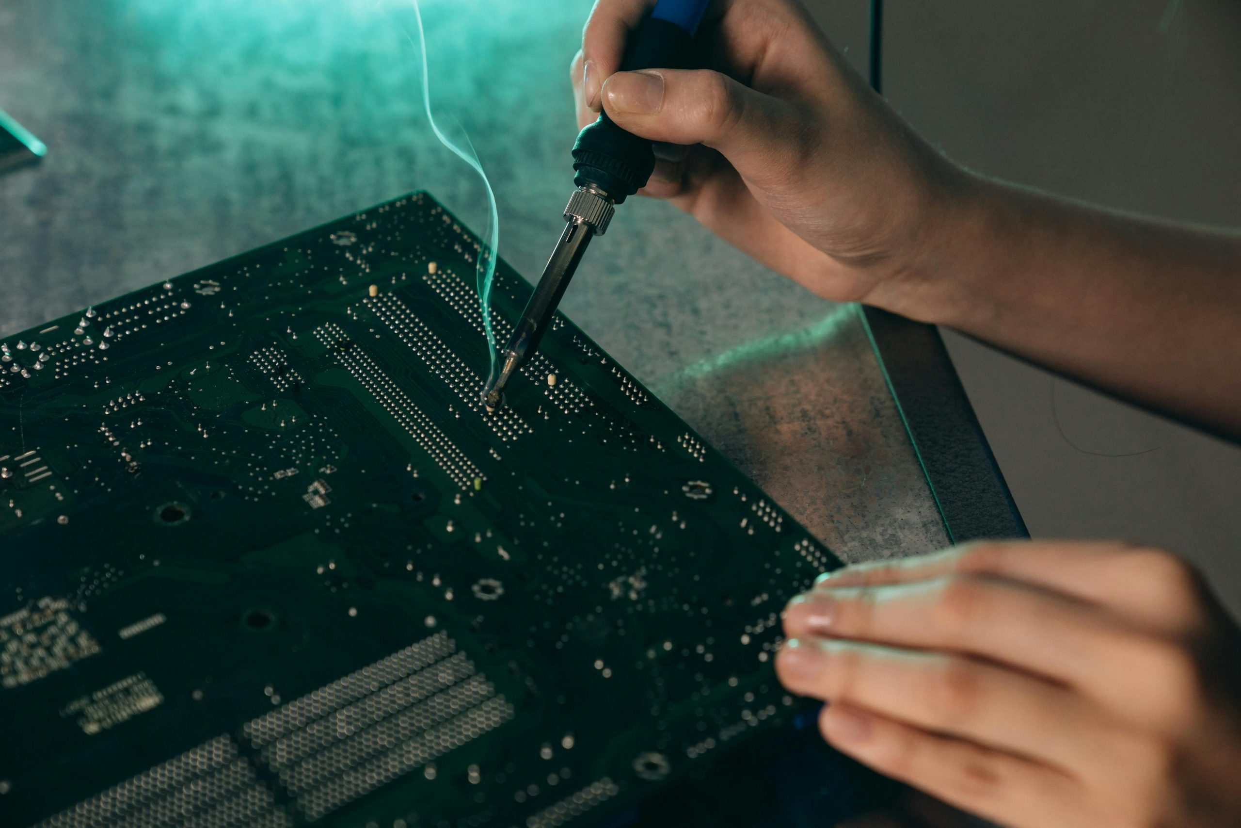 Home Close-up of hands soldering components on a motherboard with a soldering iron.